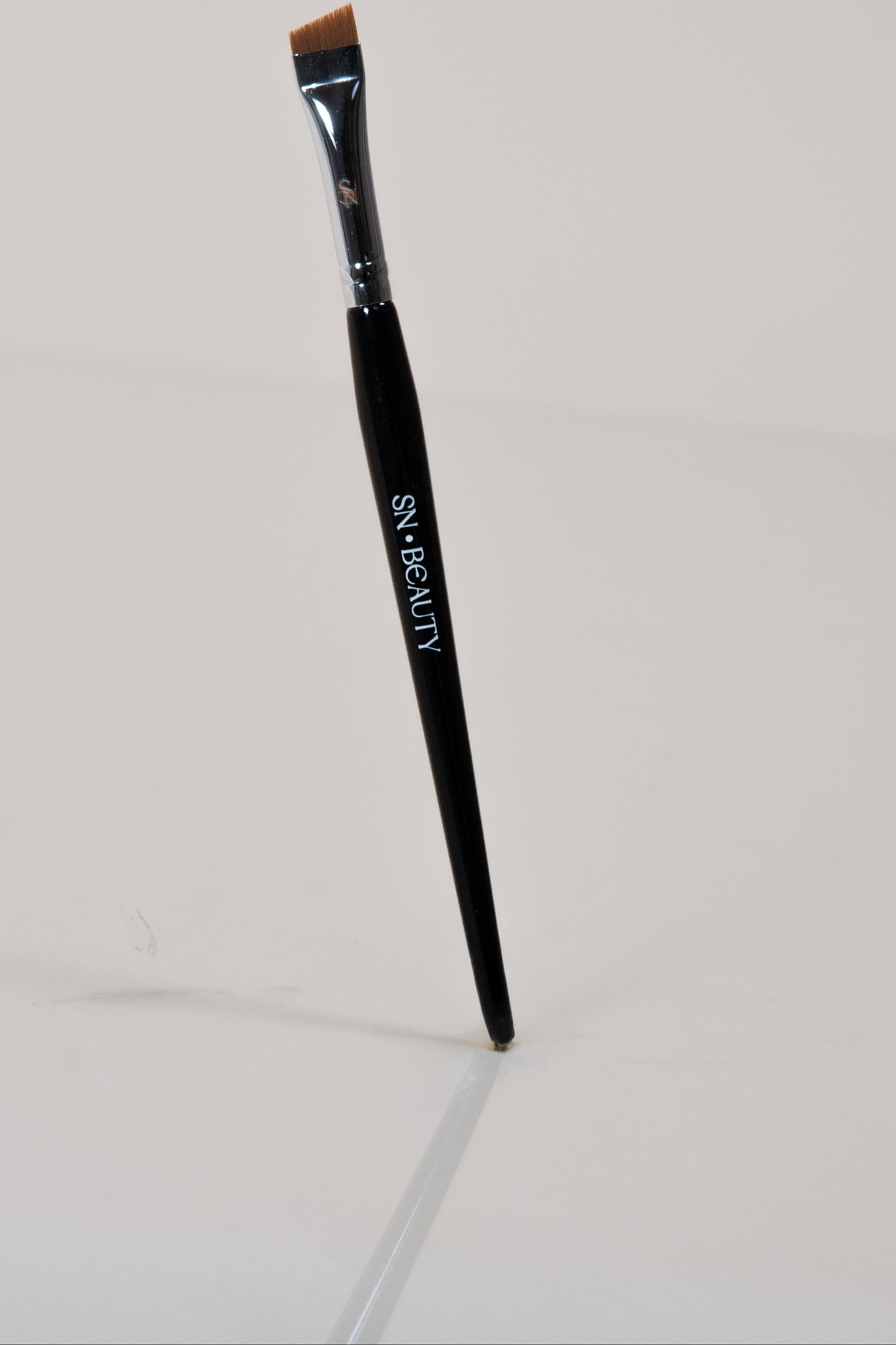 Pinceau biseauté noir SN BEAUTY posé verticalement sur fond clair, manche brillant avec logo blanc.