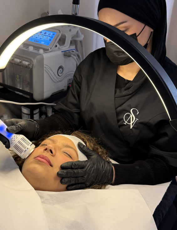 Soin du visage en institut SN Beauté, praticienne en blouse noire effectuant un traitement professionnel sous lampe LED.